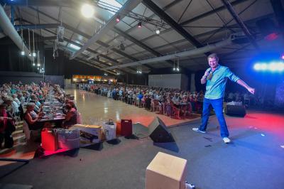 Un groupe de personnes photographiant un grand gâteau décoré, dans une salle remplie lors d'un événement festif.