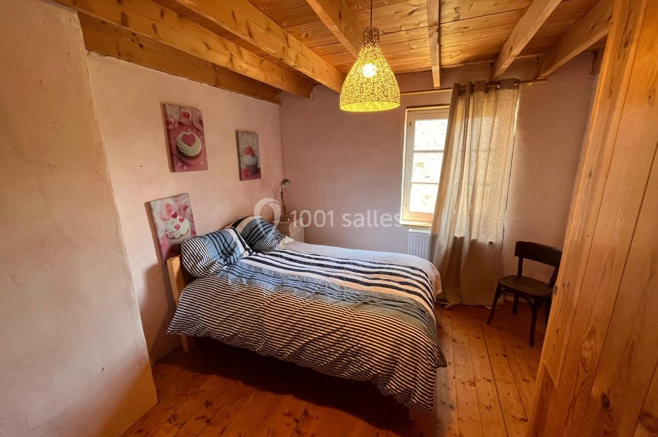 Chambre avec lit double, murs en crépi rose, plafond en bois, parquet, lampe suspendue et fenêtre avec rideau beige.