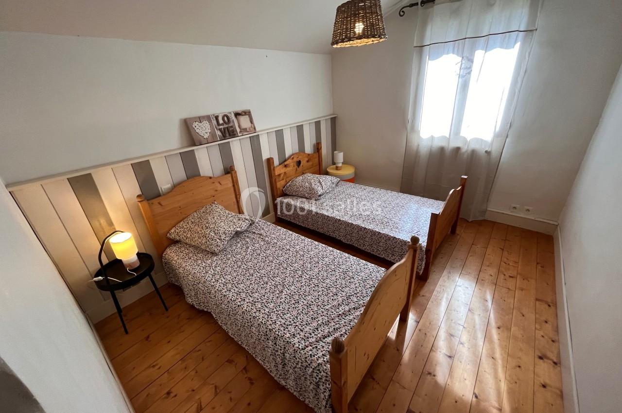 Deux lits simples en bois avec couvre-lits fleuris dans une chambre lumineuse au sol en parquet.