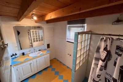 Salle de bain avec plafond en bois, carrelage coloré, douche avec rideau et lavabo sur meuble blanc.