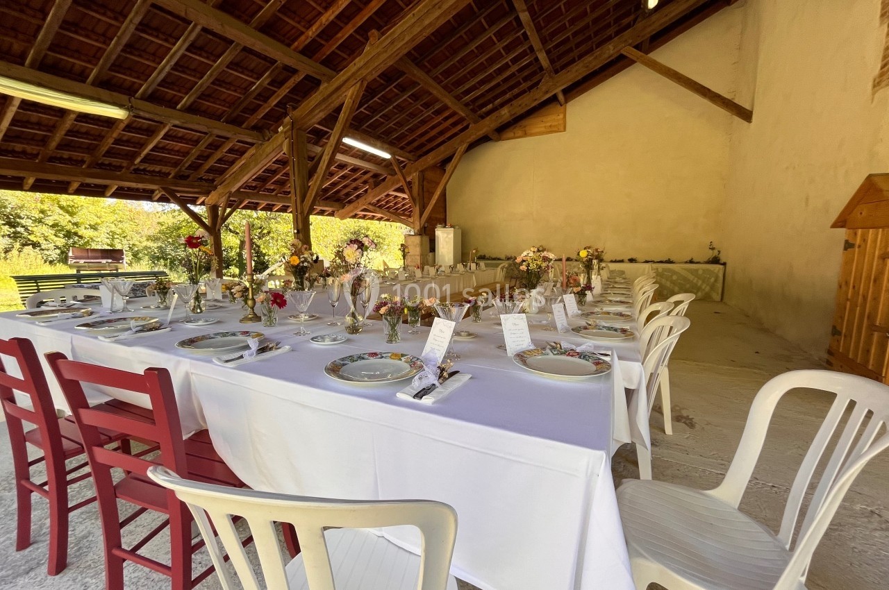 Table dressée pour un repas festif sous une charpente en bois, décorée de fleurs et de menus individuels.