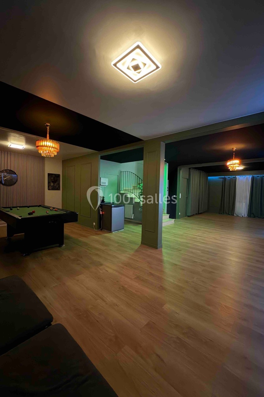 Salle spacieuse avec parquet, table de billard, éclairage moderne et rideaux sombres couvrant les fenêtres.