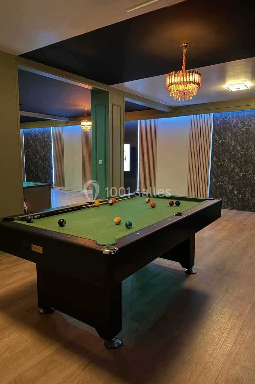 Table de billard avec boules colorées dans une pièce élégante, éclairée par des lustres et des lumières tamisées.