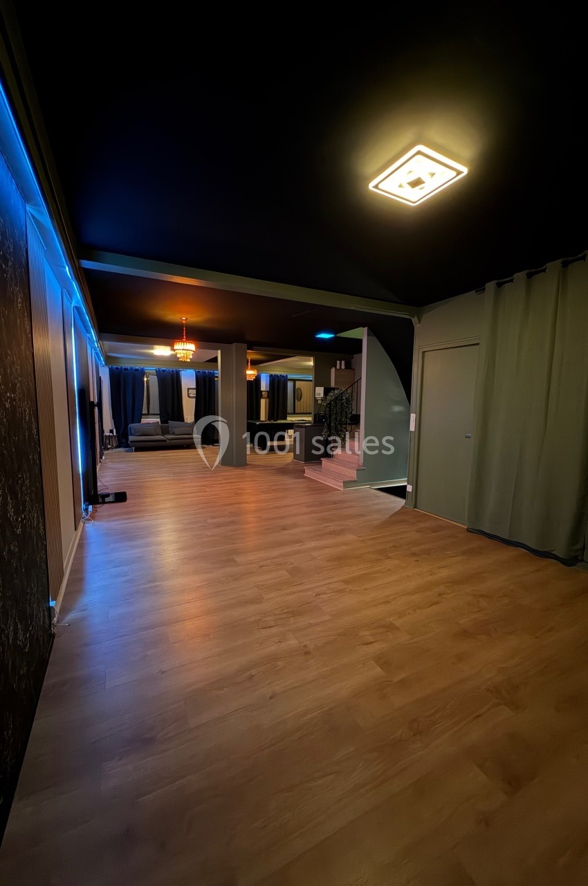 Salle intérieure avec parquet clair, murs sombres, éclairage tamisé et rideaux couvrant des ouvertures.