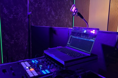 Poste de DJ avec platines, table de mixage et ordinateur portable dans une ambiance lumineuse violette et verte.