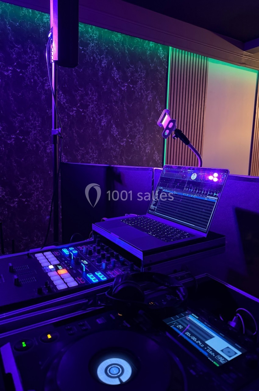 Poste de DJ avec platines, table de mixage et ordinateur portable dans une ambiance lumineuse violette et verte.