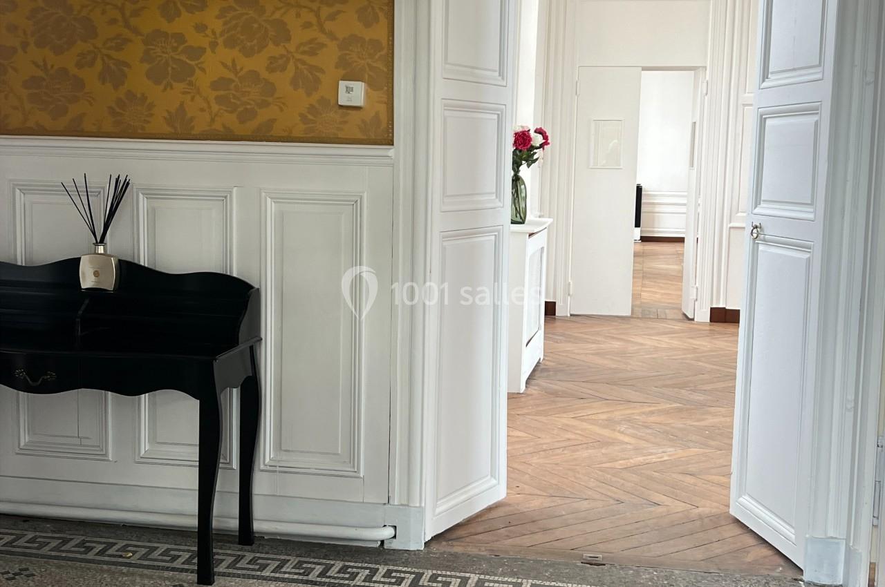 Vue d'un intérieur lumineux avec un sol en mosaïque, un bureau noir et une enfilade de portes ouvertes.
