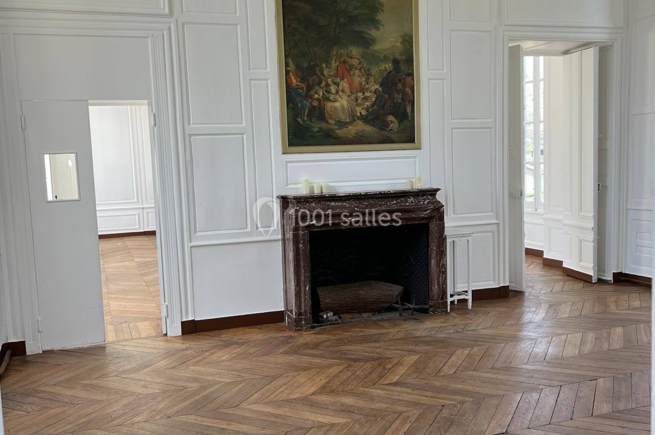 Salle lumineuse avec parquet en bois, cheminée en marbre, tableau au mur et moulures blanches sur les murs.