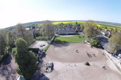 Vue aérienne d'un centre équestre avec une carrière, des cavaliers à cheval et des champs en arrière-plan.