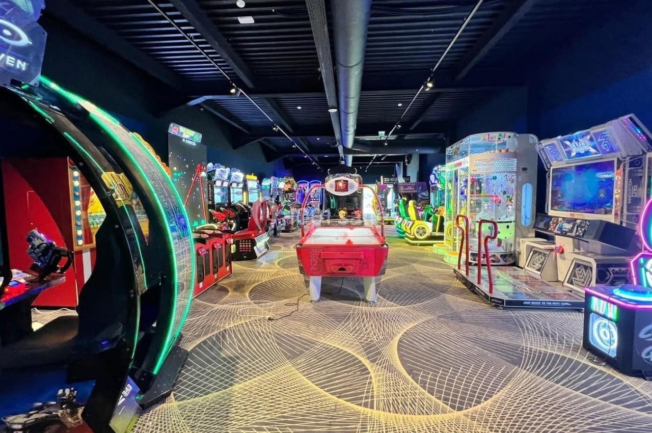 Salle d'arcade avec divers jeux vidéo, machines interactives et éclairages colorés dans un espace moderne.