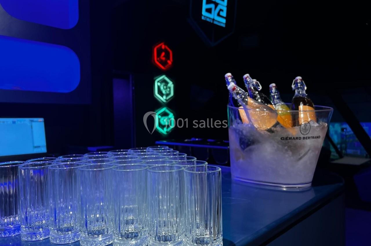 Des verres vides alignés sur un comptoir avec un seau rempli de bouteilles dans un décor lumineux.