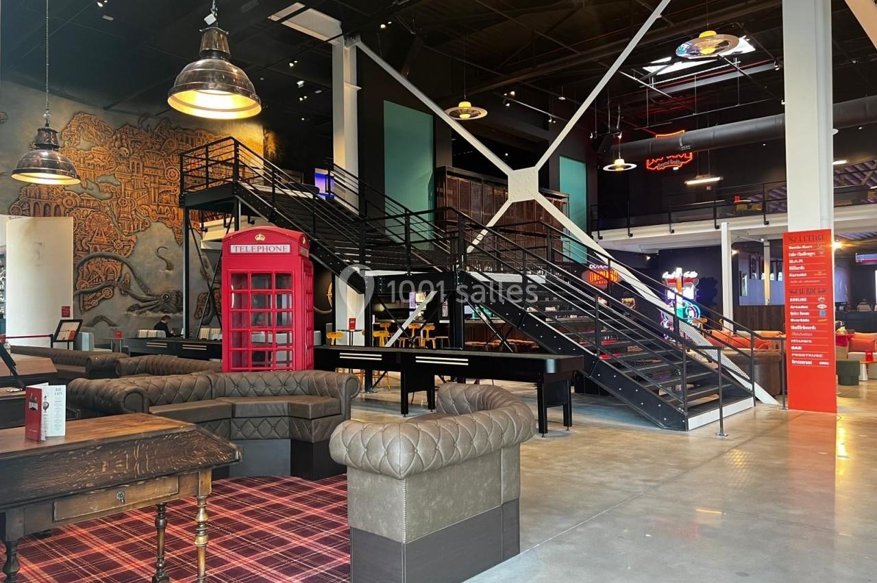 Espace intérieur avec canapés en cuir, cabine téléphonique rouge, escalier métallique et décorations modernes.