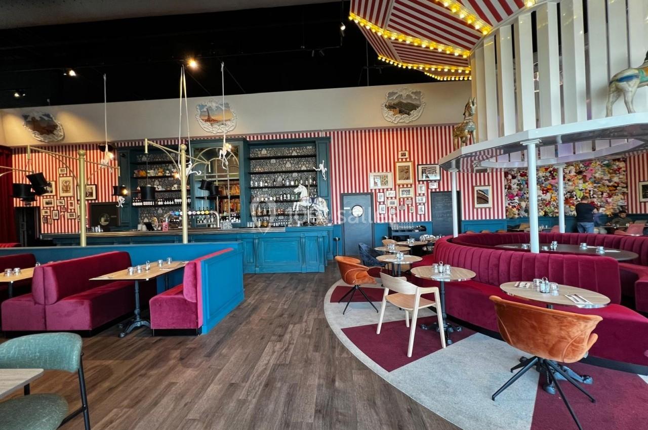 Intérieur d'un restaurant coloré avec banquettes rouges, chaises orange, bar en arrière-plan et décorations murales variées.