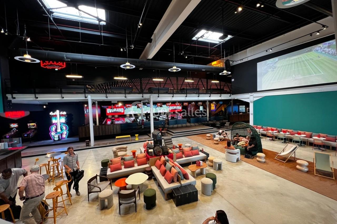 Espace intérieur moderne avec coin salon, jeux d'arcade, écran géant diffusant un match et ambiance conviviale.