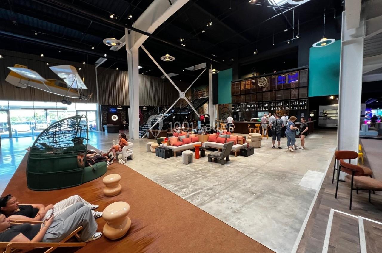 Espace intérieur moderne avec mobilier varié, coin salon coloré, mezzanine et éclairage naturel provenant d'une verrière.