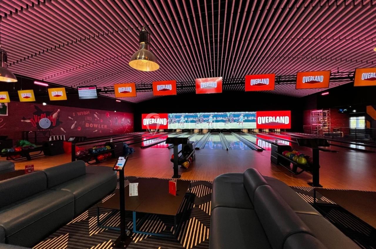 Salle de bowling moderne avec plusieurs pistes, éclairage coloré et écrans affichant le logo ’Overland’.