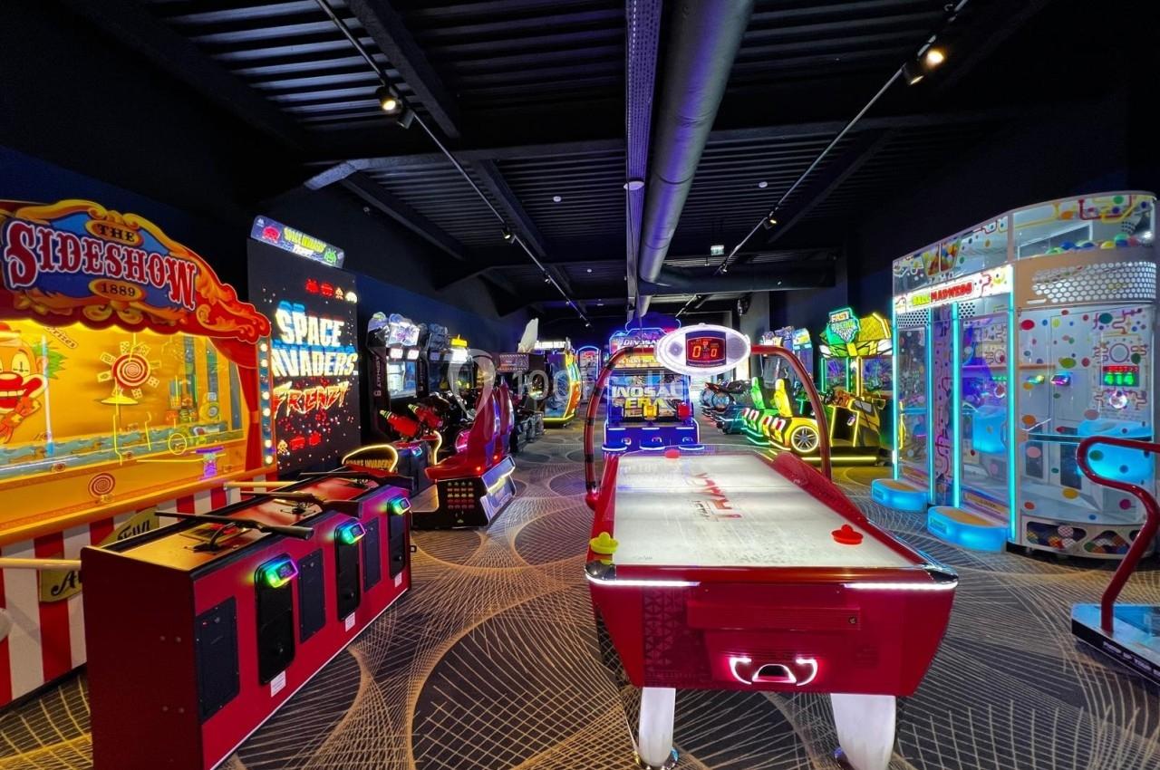 Salle d'arcade colorée avec divers jeux interactifs, machines rétro et table de air hockey illuminée.
