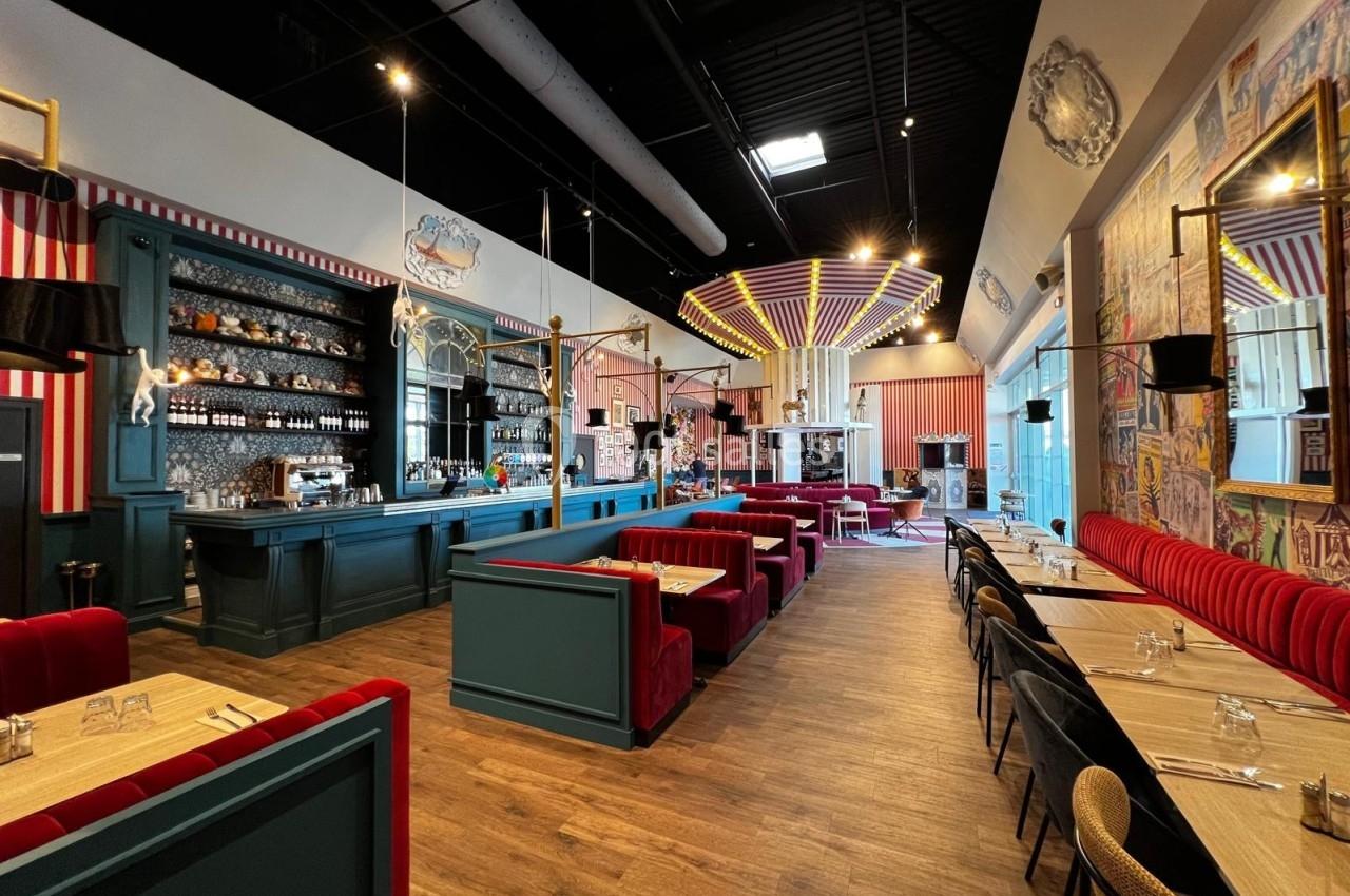 Intérieur d'un restaurant avec banquettes rouges, tables en bois, bar central et décoration colorée et éclectique.