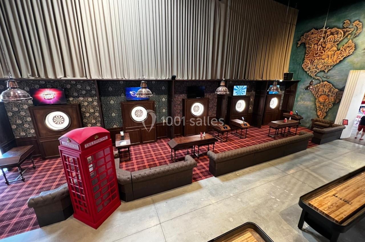Salle de jeux avec cibles de fléchettes, canapés, cabine téléphonique rouge et décor mural coloré.