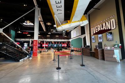 Un avion jaune suspendu au plafond d'un hall spacieux avec un comptoir d'accueil et des baies vitrées.