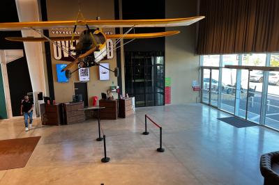 Un avion jaune suspendu au plafond d'un hall spacieux avec un comptoir d'accueil et des baies vitrées.