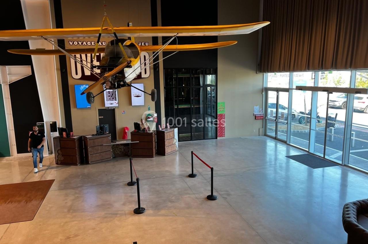 Un avion jaune suspendu au plafond d'un hall spacieux avec un comptoir d'accueil et des baies vitrées.