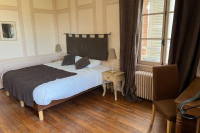 Chambre lumineuse avec lit double, draps blancs, coussins gris, bureau en bois et parquet en bois clair.