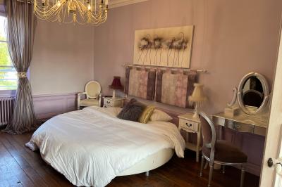 Chambre lumineuse avec lit double, draps blancs, coussins gris, bureau en bois et parquet en bois clair.