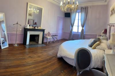 Chambre lumineuse avec lit double, draps blancs, coussins gris, bureau en bois et parquet en bois clair.