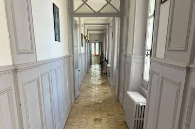 Chambre lumineuse avec lit double, draps blancs, coussins gris, bureau en bois et parquet en bois clair.