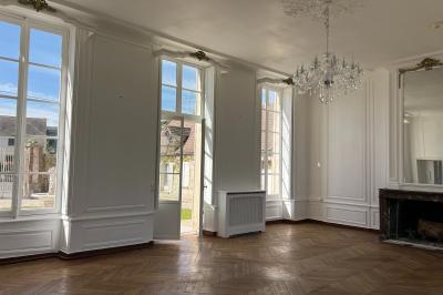 Chambre lumineuse avec lit double, draps blancs, coussins gris, bureau en bois et parquet en bois clair.