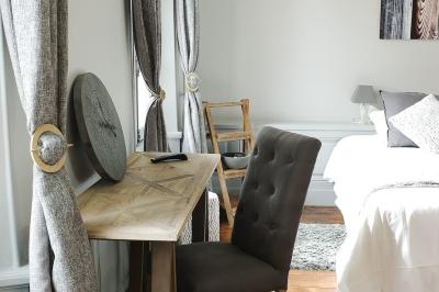 Chambre lumineuse avec lit double, draps blancs, coussins gris, bureau en bois et parquet en bois clair.