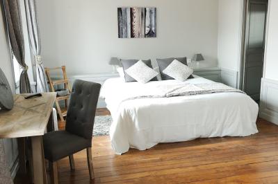 Chambre lumineuse avec lit double, draps blancs, coussins gris, bureau en bois et parquet en bois clair.