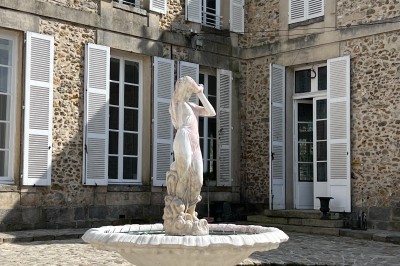 Chambre lumineuse avec lit double, draps blancs, coussins gris, bureau en bois et parquet en bois clair.