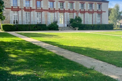 Chambre lumineuse avec lit double, draps blancs, coussins gris, bureau en bois et parquet en bois clair.