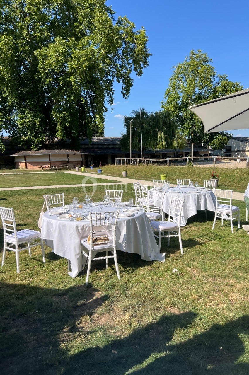 Tables rondes dressées avec nappes blanches et chaises blanches sur une pelouse, sous un ciel dégagé.