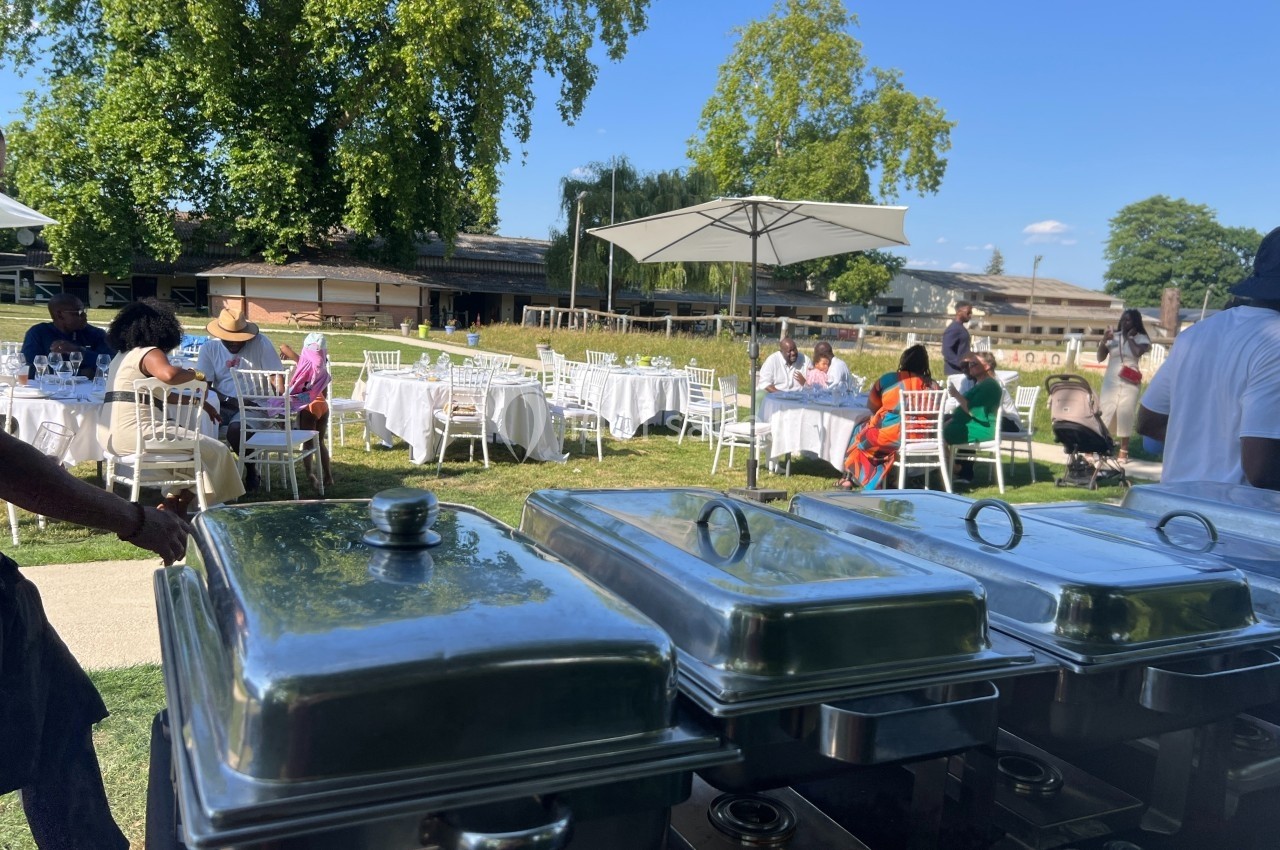 Buffet en plein air avec des tables dressées et des invités assis dans un jardin sous un ciel ensoleillé.