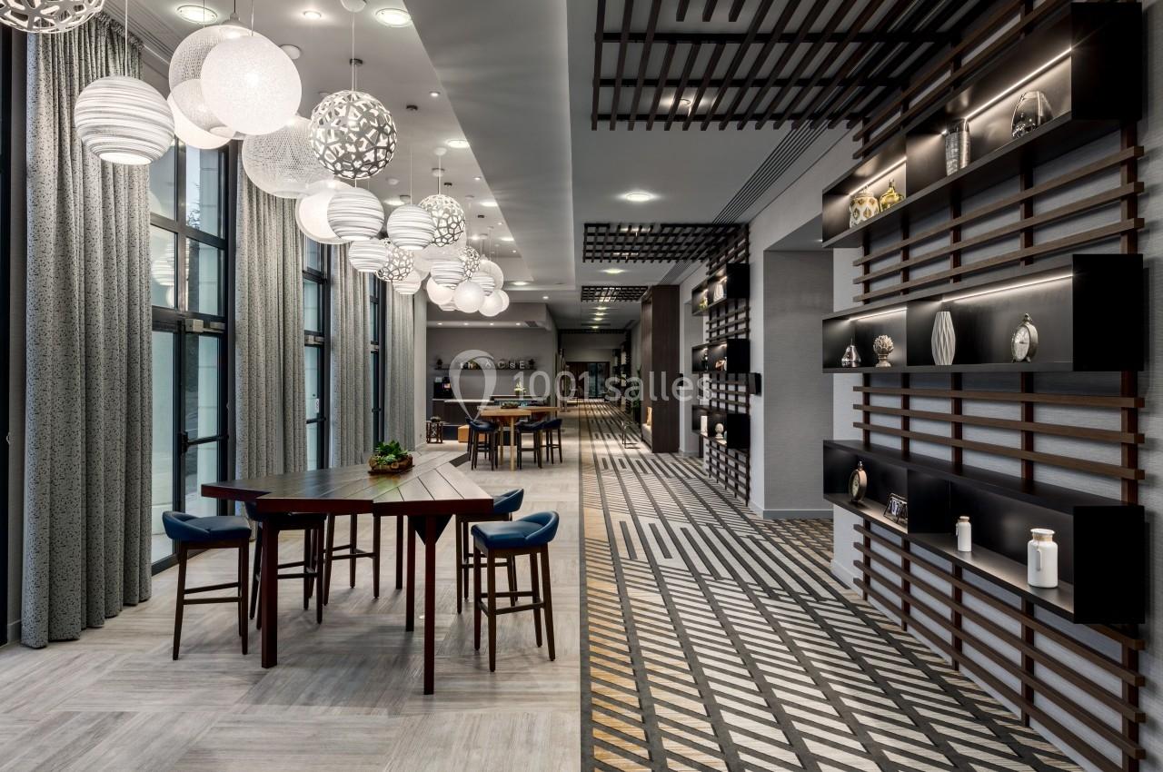 Salle moderne avec tables en bois, chaises rembourrées, luminaires suspendus et étagères décoratives sur les murs.