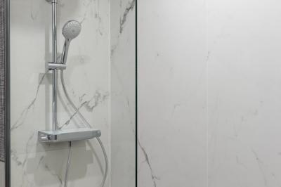 Salle de bain moderne avec lavabo en marbre, miroir éclairé, accessoires de toilette et douche en arrière-plan.