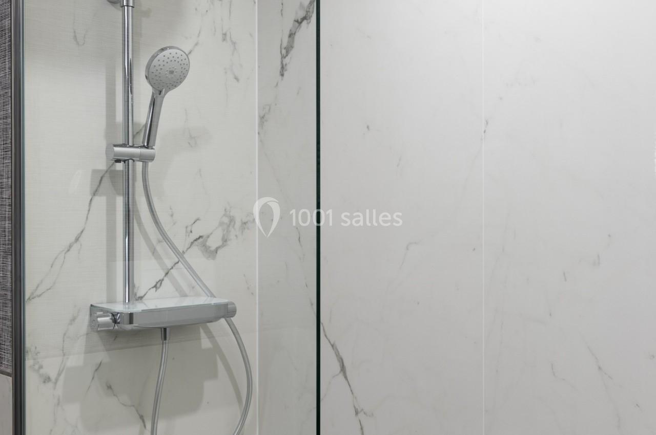 Douche moderne avec paroi en verre, pommeau fixe et mobile, sur fond de carrelage effet marbre blanc.