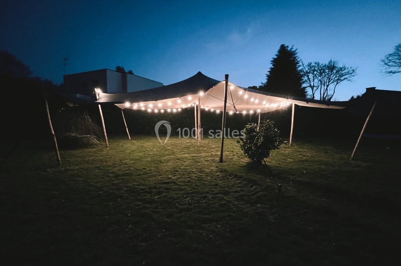 Tente éclairée par des guirlandes lumineuses dans un jardin au crépuscule.