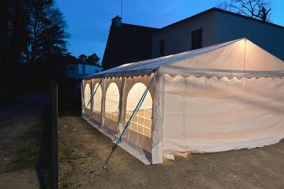 Tente beige éclairée par des guirlandes lumineuses, installée dans un jardin au coucher du soleil.
