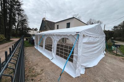 Tente beige éclairée par des guirlandes lumineuses, installée dans un jardin au coucher du soleil.