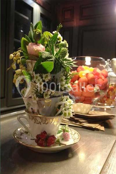 Empilement de tasses en porcelaine garnies de fleurs et feuillages, posé sur une table près d'un bol de fruits rouges.