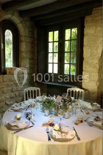 Table ronde élégamment dressée avec vaisselle raffinée, décorations florales et lumière naturelle entrant par une fenêtre.