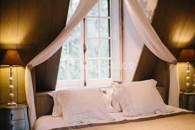 Lit double avec draps blancs, plaid bleu et tables de chevet avec lampes dans une chambre à la décoration rustique.