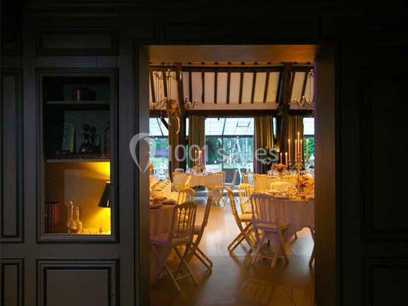 Salle de réception élégante avec tables dressées, chaises blanches et lumière tamisée provenant des chandeliers.