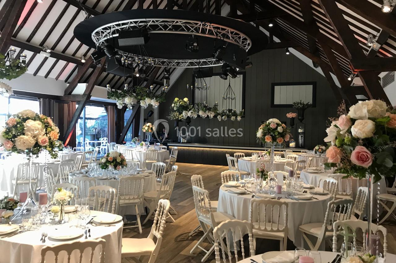 Salle de réception décorée avec des tables rondes, des chaises blanches et des compositions florales élégantes.
