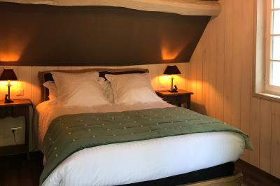 Lit double avec draps blancs, plaid bleu et tables de chevet avec lampes dans une chambre à la décoration rustique.