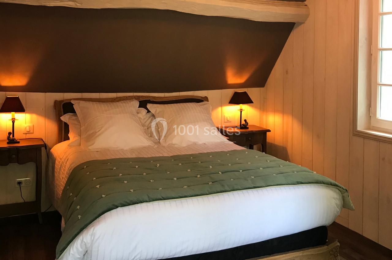 Lit double avec couverture verte dans une chambre mansardée en bois, éclairée par des lampes de chevet.